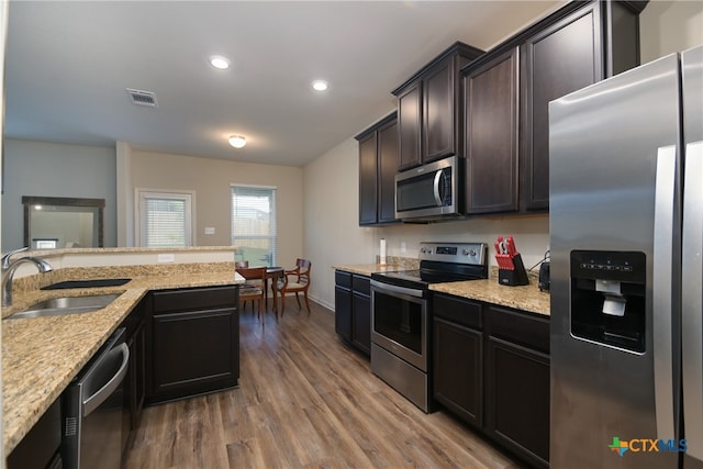 kitchen featuring hardwood / wood-style floors, sink, light stone countertops, dark brown cabinets, and appliances with stainless steel finishes