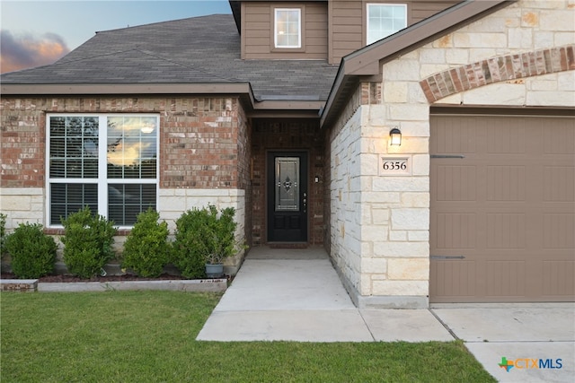 exterior entry at dusk featuring a garage and a lawn