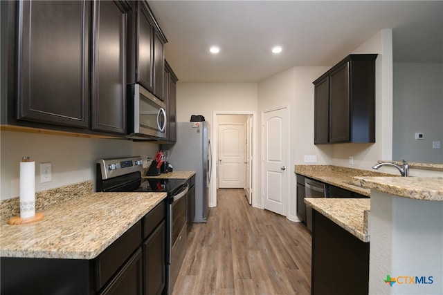 kitchen with stainless steel appliances, sink, light stone countertops, dark brown cabinets, and light wood-type flooring