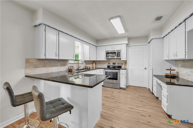 kitchen with sink, kitchen peninsula, appliances with stainless steel finishes, dark stone counters, and light wood-type flooring