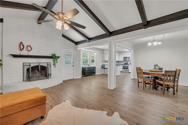 living room featuring lofted ceiling with beams, hardwood / wood-style floors, a brick fireplace, and ceiling fan with notable chandelier