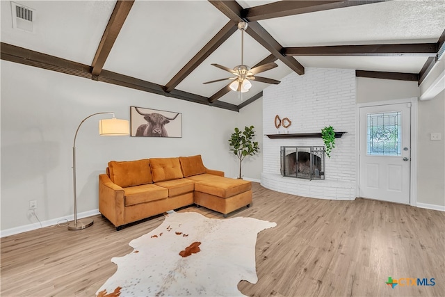 living room featuring lofted ceiling with beams, light hardwood / wood-style flooring, ceiling fan, and a fireplace