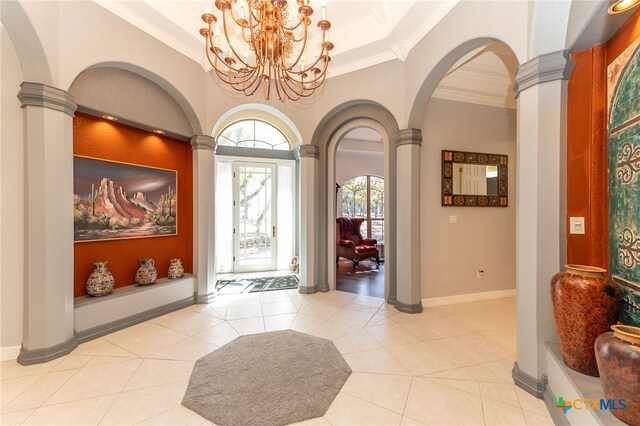 tiled foyer featuring decorative columns, an inviting chandelier, and ornamental molding