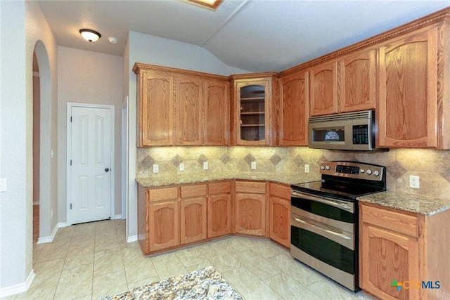 kitchen featuring appliances with stainless steel finishes, tasteful backsplash, glass insert cabinets, and light stone countertops