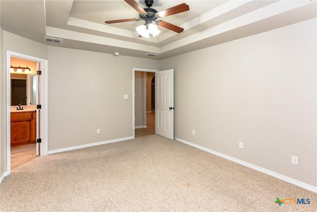 unfurnished bedroom featuring a tray ceiling, visible vents, a sink, and baseboards