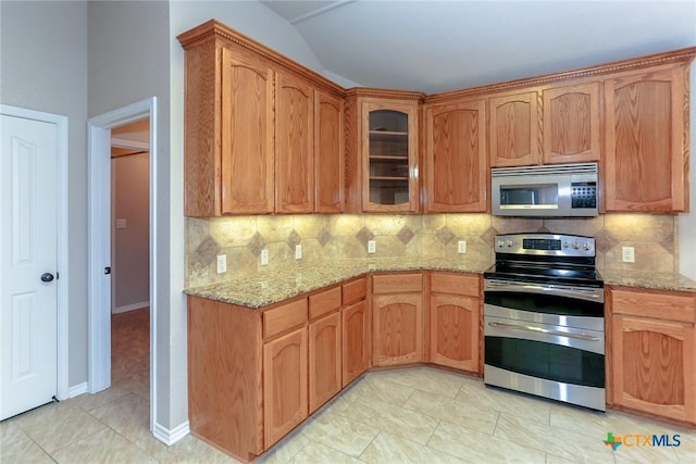 kitchen featuring appliances with stainless steel finishes, decorative backsplash, glass insert cabinets, and light stone countertops