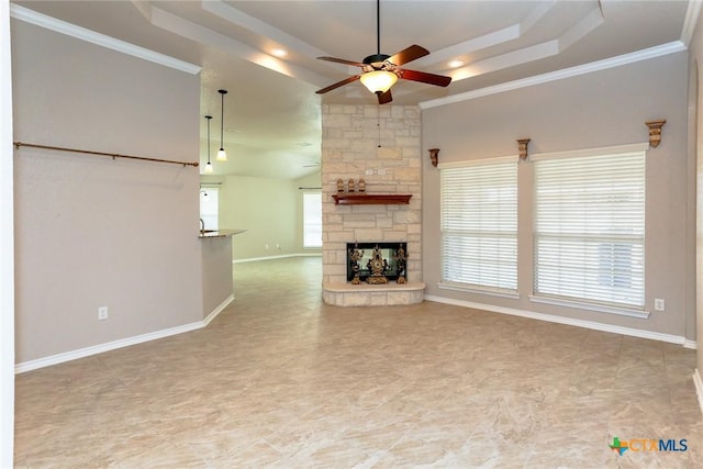 unfurnished living room with baseboards, a raised ceiling, ceiling fan, crown molding, and a fireplace