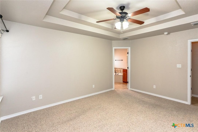 unfurnished bedroom with ensuite bath, baseboards, a tray ceiling, and light colored carpet