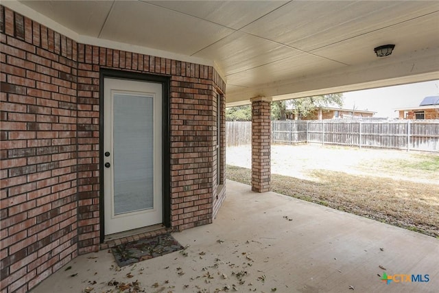 doorway to property with fence, a patio, and brick siding