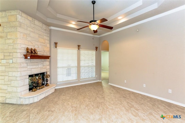 unfurnished living room with arched walkways, a fireplace, a raised ceiling, ceiling fan, and baseboards