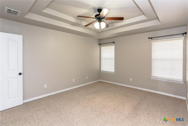 empty room with ceiling fan, a raised ceiling, visible vents, and baseboards