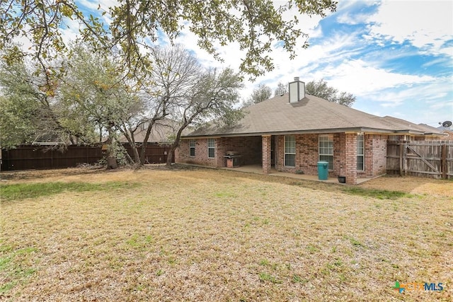 back of house featuring a fenced backyard, brick siding, a lawn, a chimney, and a patio area