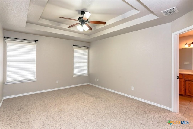 spare room featuring a tray ceiling, a ceiling fan, visible vents, and baseboards