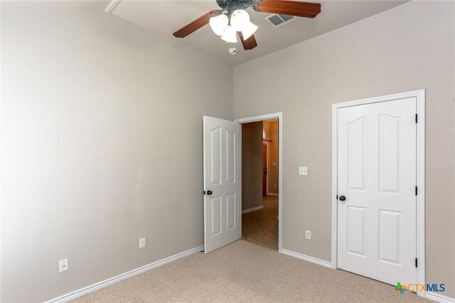 unfurnished bedroom with visible vents, light carpet, vaulted ceiling, ceiling fan, and baseboards