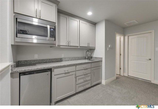 kitchen with light stone counters, gray cabinets, appliances with stainless steel finishes, light carpet, and sink