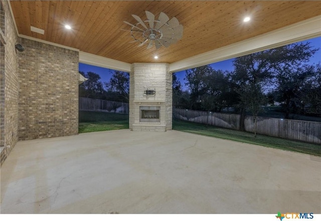 patio terrace at dusk featuring an outdoor stone fireplace and ceiling fan