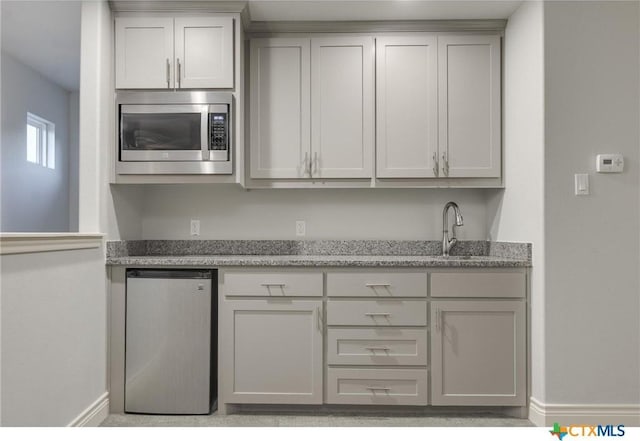 kitchen featuring stainless steel appliances, stone countertops, gray cabinetry, and sink