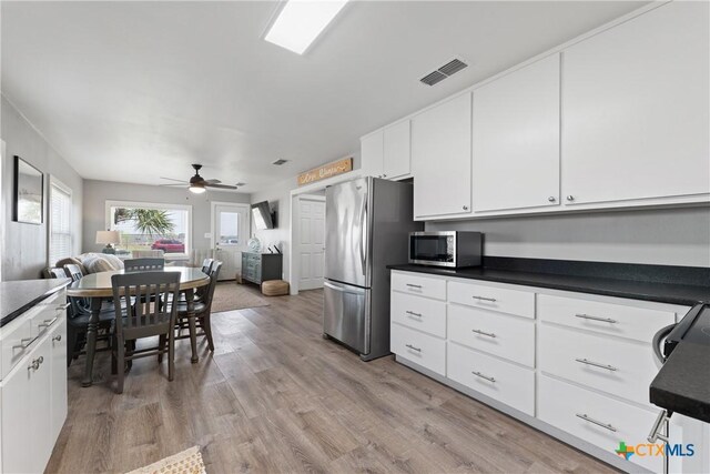 1113 W Port Dr, Port Mansfield, TX 78598 - kitchen featuring stainless steel appliances, open floor plan, dark countertops, ceiling fan, and light wood finished floors
