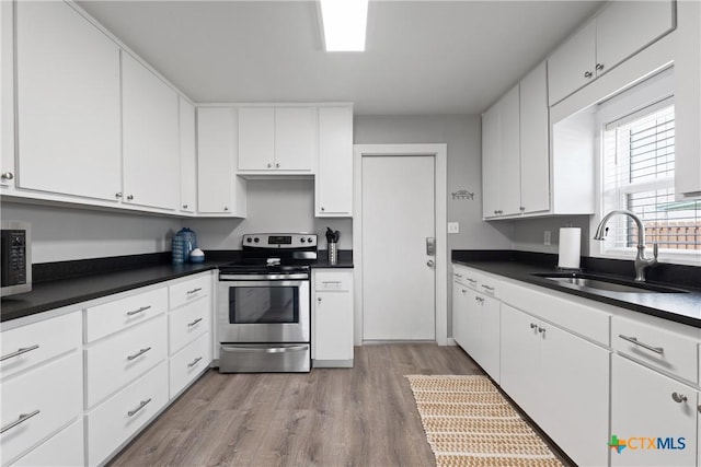1113 W Port Dr, Port Mansfield, TX 78598 - kitchen featuring stainless steel range with electric stovetop, light wood-type flooring, dark countertops, and white cabinets