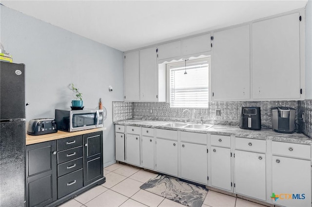 kitchen with white cabinets, black refrigerator, light tile patterned flooring, and sink