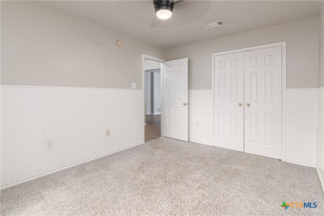 unfurnished bedroom featuring carpet, a closet, visible vents, wainscoting, and ceiling fan