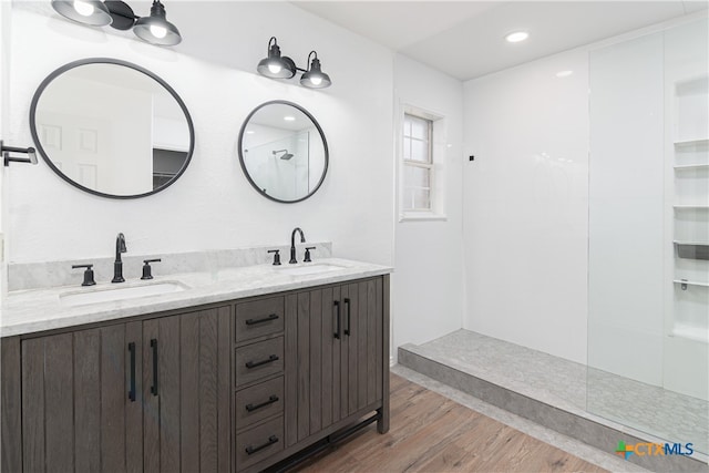 full bath with double vanity, walk in shower, a sink, and wood finished floors