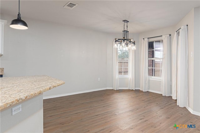 unfurnished dining area with light wood finished floors, baseboards, visible vents, and an inviting chandelier