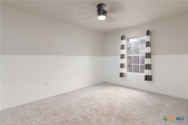 carpeted spare room with a wainscoted wall and a ceiling fan