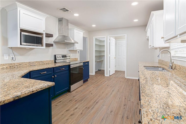 kitchen with visible vents, wall chimney exhaust hood, appliances with stainless steel finishes, blue cabinetry, and a sink