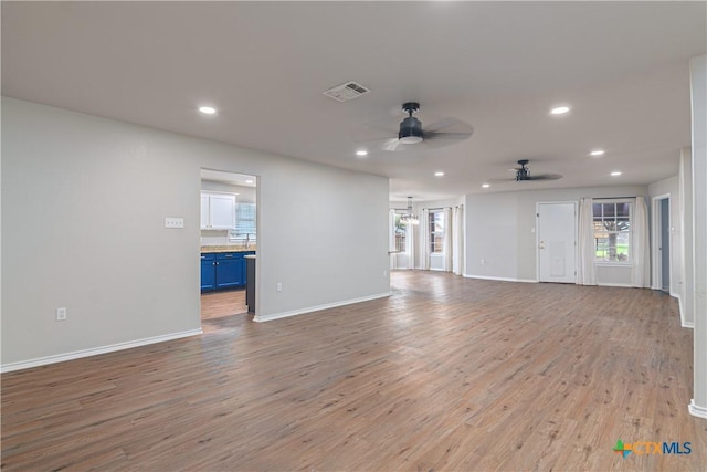 unfurnished living room with light wood finished floors, recessed lighting, visible vents, baseboards, and ceiling fan with notable chandelier