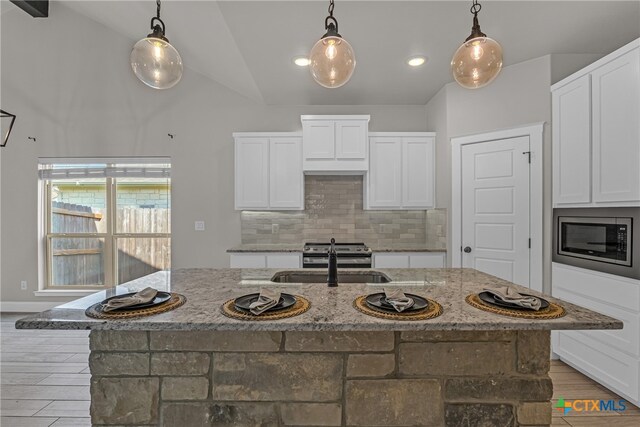 kitchen with a center island with sink, white cabinetry, appliances with stainless steel finishes, hanging light fixtures, and vaulted ceiling