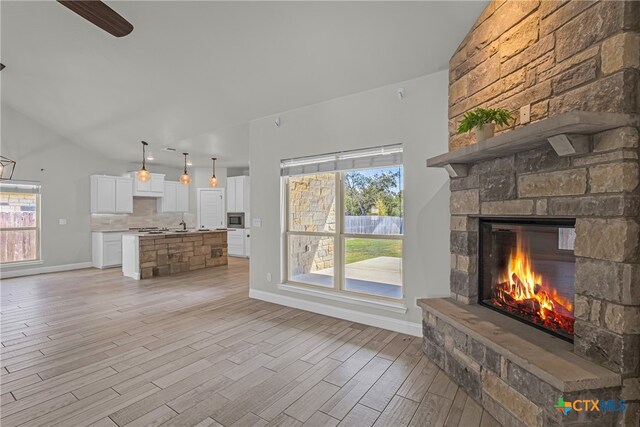 unfurnished living room with light hardwood / wood-style floors, a stone fireplace, and vaulted ceiling