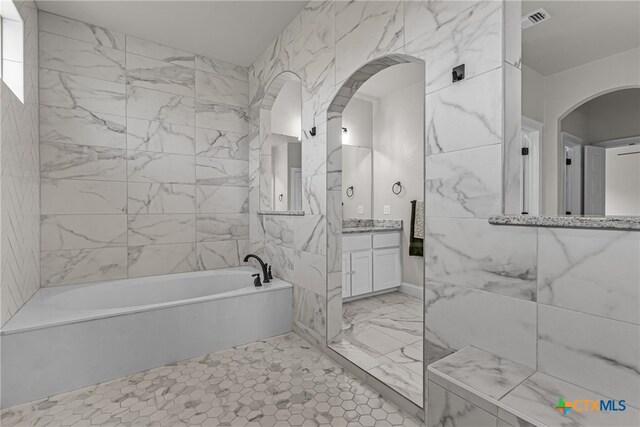 bathroom featuring tile walls, a tub to relax in, and vanity