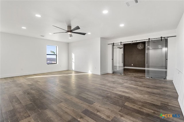 unfurnished bedroom featuring dark wood-type flooring, ceiling fan, and a barn door