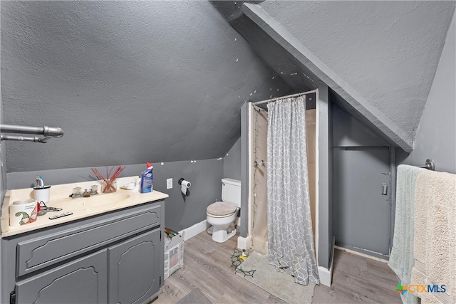 bathroom with a shower with shower curtain, vanity, vaulted ceiling, hardwood / wood-style floors, and toilet