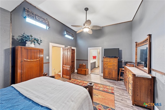 bedroom with ceiling fan, a towering ceiling, ensuite bathroom, and light wood-type flooring