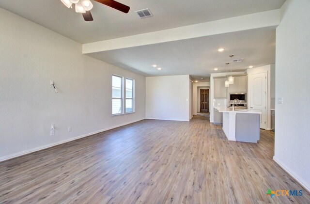 unfurnished living room with ceiling fan, light wood-type flooring, and sink