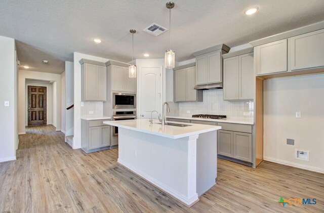 kitchen with appliances with stainless steel finishes, light hardwood / wood-style floors, gray cabinets, and tasteful backsplash