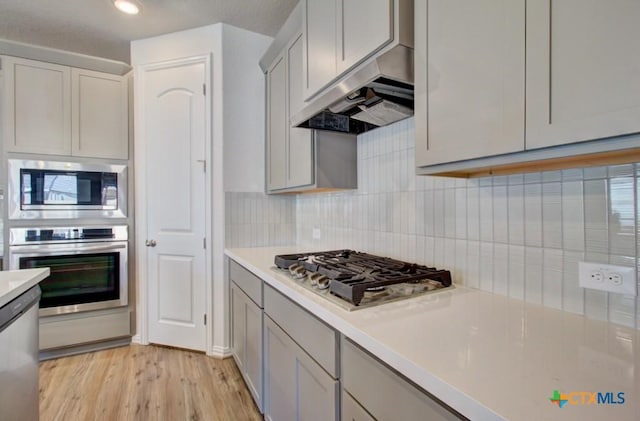 kitchen with backsplash, light wood-type flooring, stainless steel appliances, and extractor fan