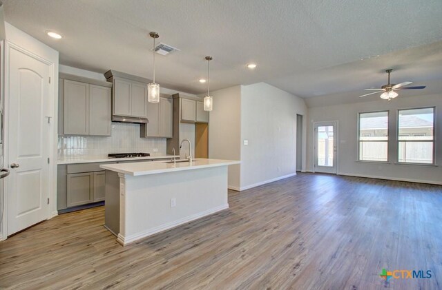 kitchen featuring gray cabinetry, sink, light hardwood / wood-style flooring, ceiling fan, and an island with sink