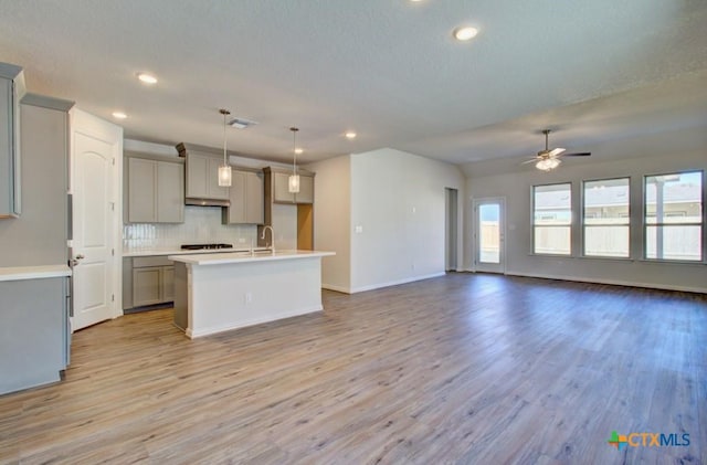 kitchen with pendant lighting, gray cabinetry, a center island with sink, and light hardwood / wood-style floors