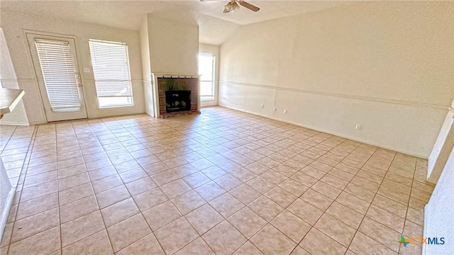 unfurnished living room featuring a brick fireplace, light tile patterned flooring, and ceiling fan