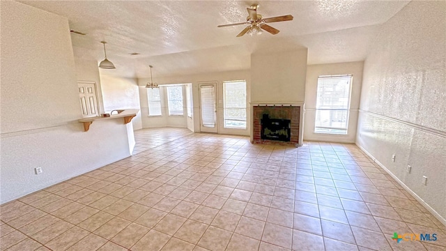 unfurnished living room featuring ceiling fan with notable chandelier, a fireplace, a textured ceiling, and light tile patterned flooring