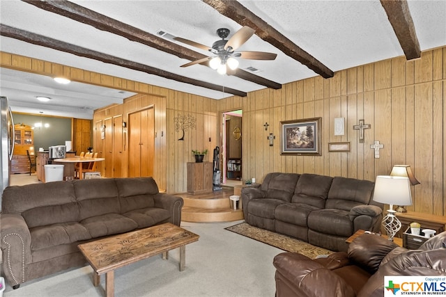 living room with wood walls, a textured ceiling, beam ceiling, and ceiling fan