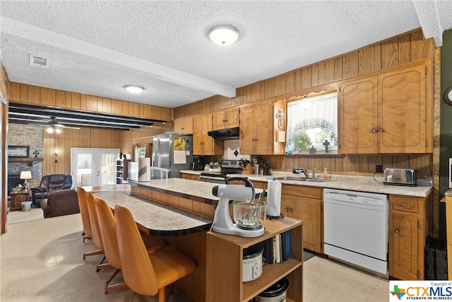 210 N 8th St, Lometa, TX 76853 - kitchen featuring stainless steel appliances, wood walls, under cabinet range hood, a textured ceiling, and light countertops