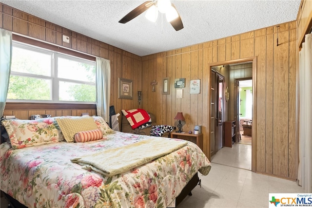 bedroom featuring ceiling fan, a textured ceiling, and wooden walls