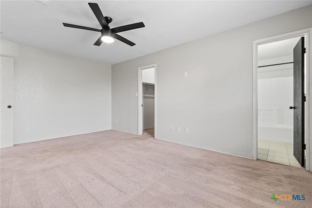 unfurnished bedroom featuring a walk in closet, carpet floors, a closet, ceiling fan, and ensuite bathroom