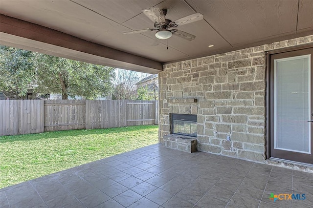 view of patio featuring a ceiling fan, an outdoor stone fireplace, and a fenced backyard