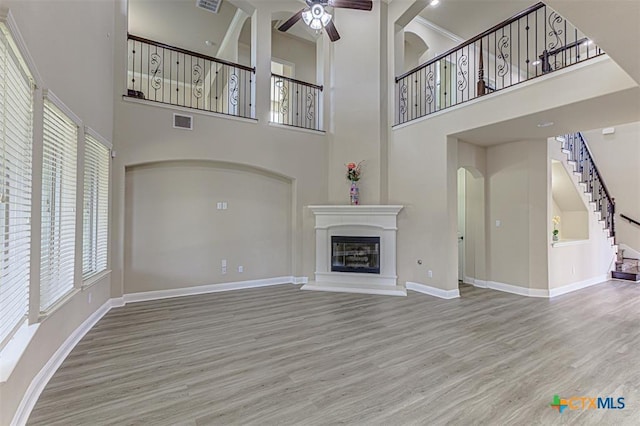 unfurnished living room featuring visible vents, baseboards, ceiling fan, wood finished floors, and a glass covered fireplace