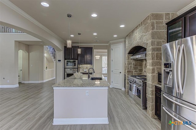 kitchen with an island with sink, light wood-style flooring, appliances with stainless steel finishes, arched walkways, and a sink